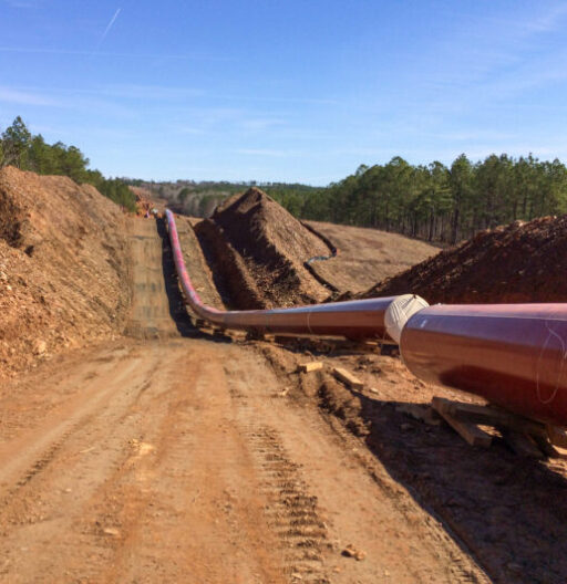 An above-ground large-diameter pipeline under construction, recedes into the distance.