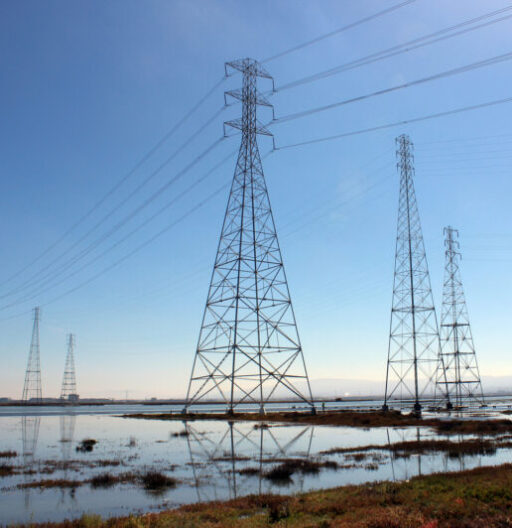 Five large electrical transmission towers spanning across a body of water.