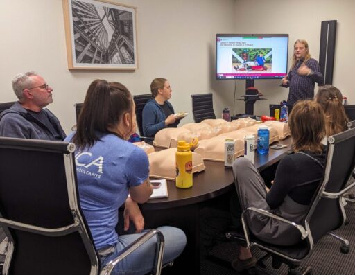Five people at a conference room table listen to a speaker.