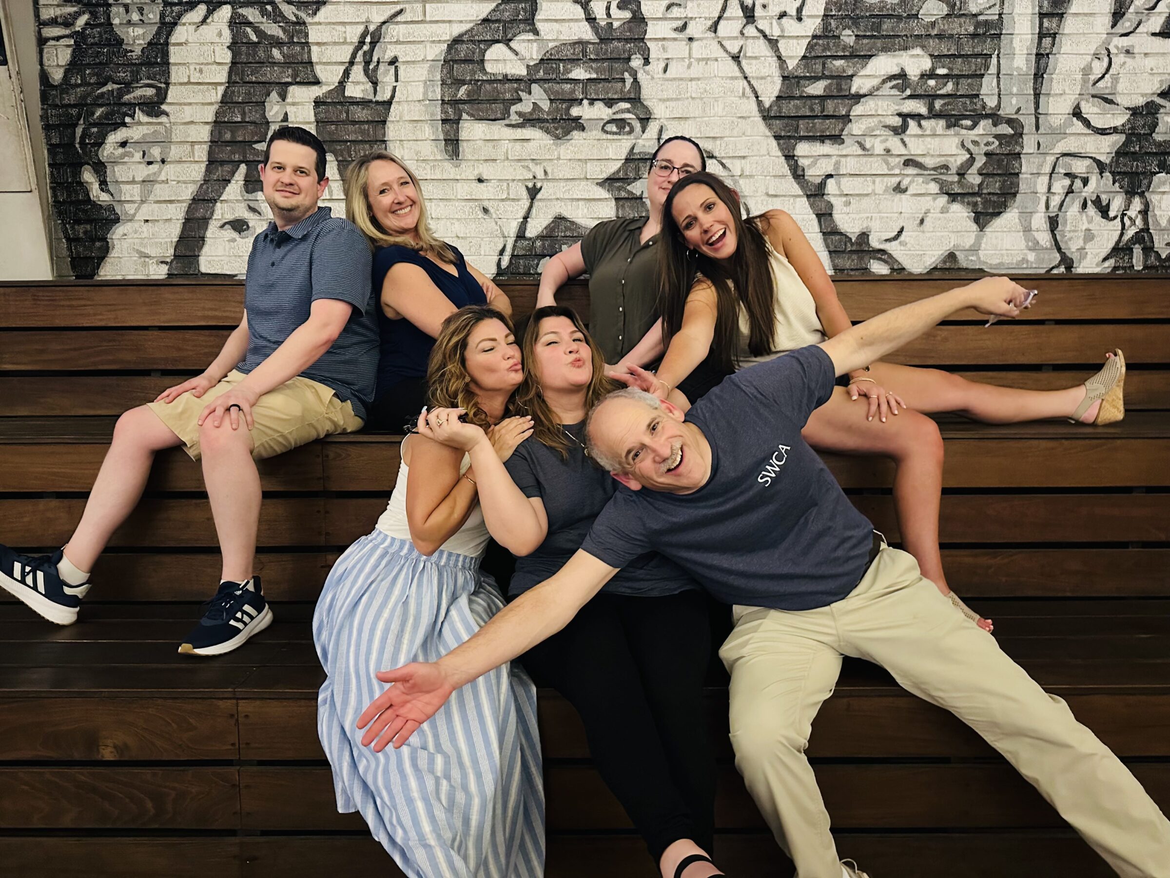 Seven people pose playfully on some wooden bleachers.