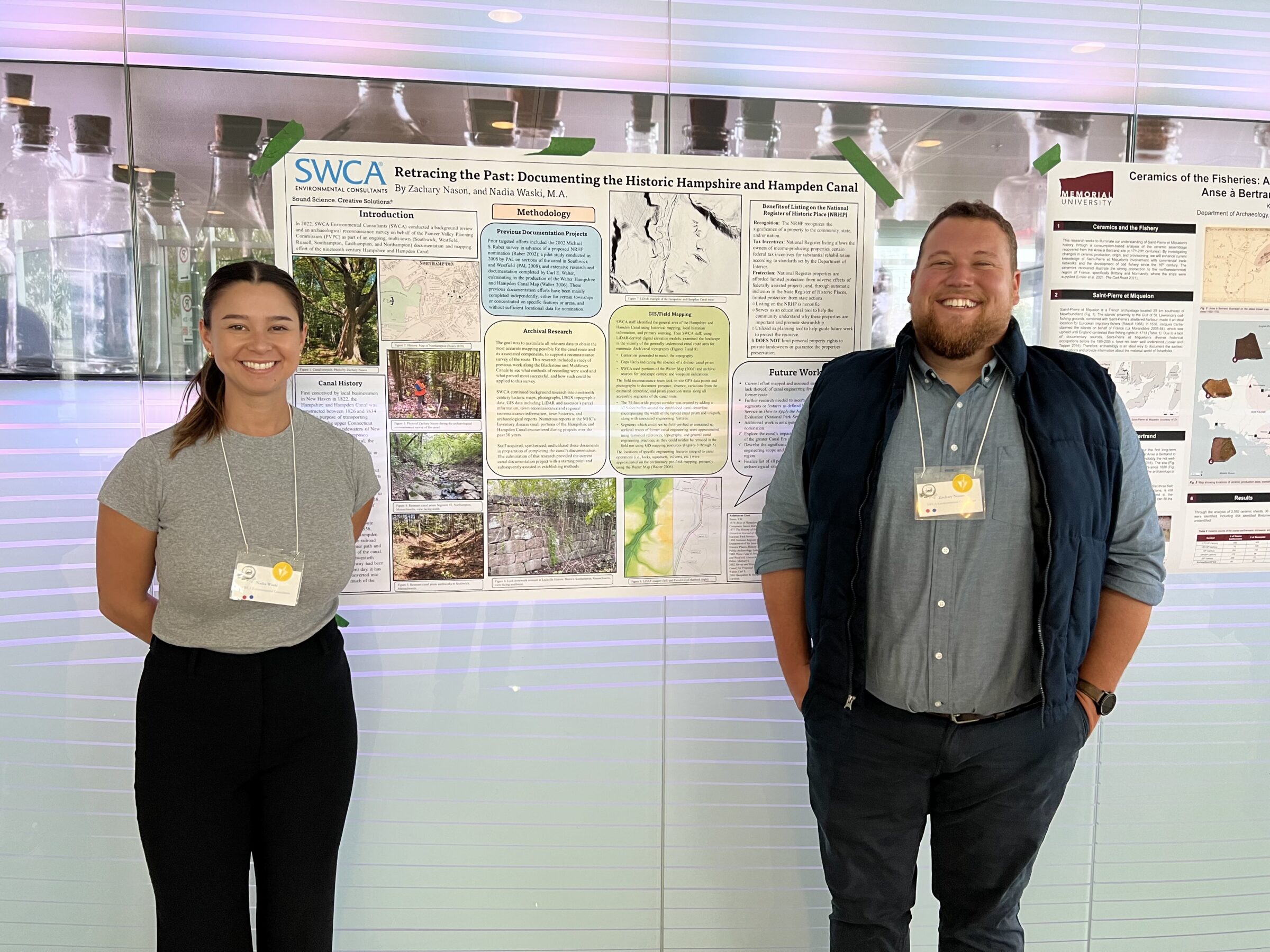 Two people pose in front of an SWCA outreach or research poster taped to the wall.