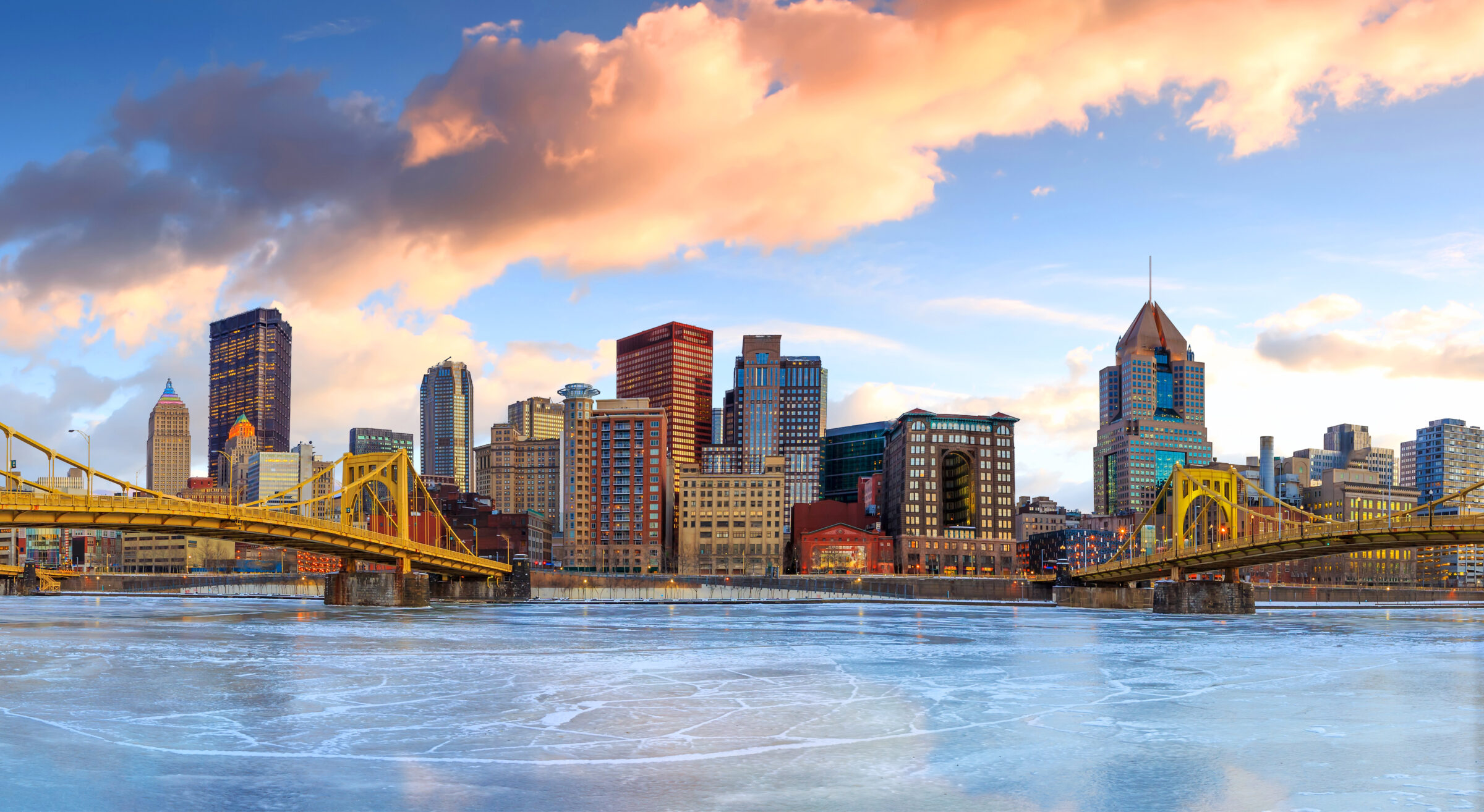 Skyline of downtown Pittsburgh at twilight panorama. Various buildings and two bridges over a body of water.