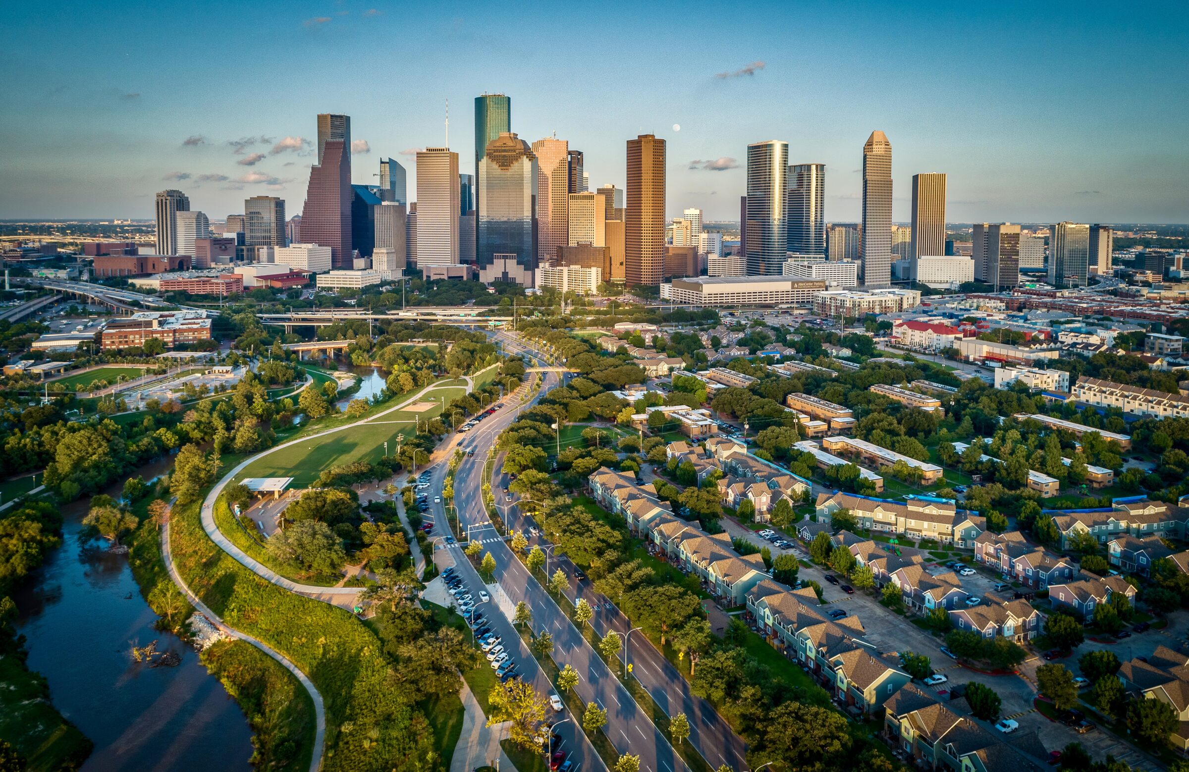 Houston, Texas Skyline At Sunset showing a stream or bayou, houses, and downtown Houston.