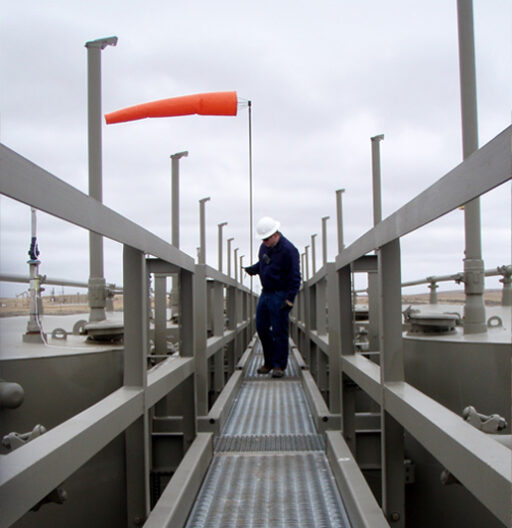 A person walks on an industrial walkway. Orange windsock is indicating wind direction.