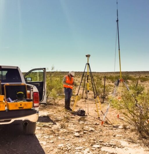 Survey tripod set up near pickup truck in open space.