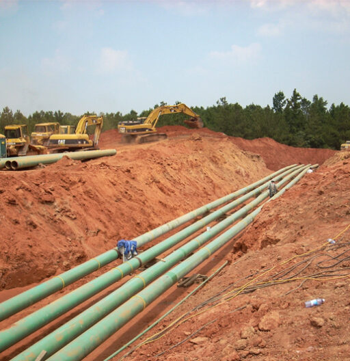 A trench is freshly dug and four green pipelines are laid inside it.