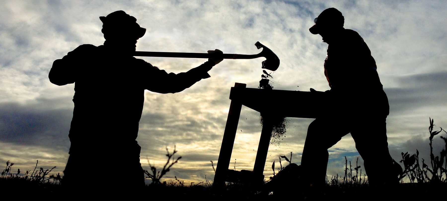 One person holding a shovel and pouring dirt through a sifter that another person is holding.