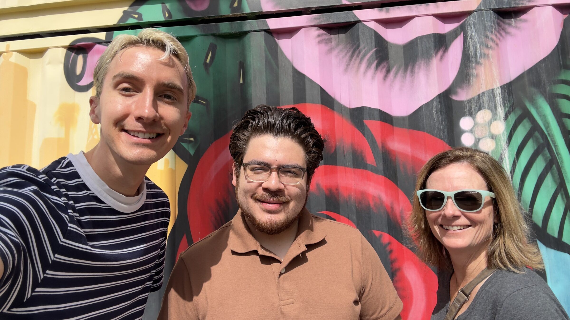 Three people posing in front of an outdoor wall mural