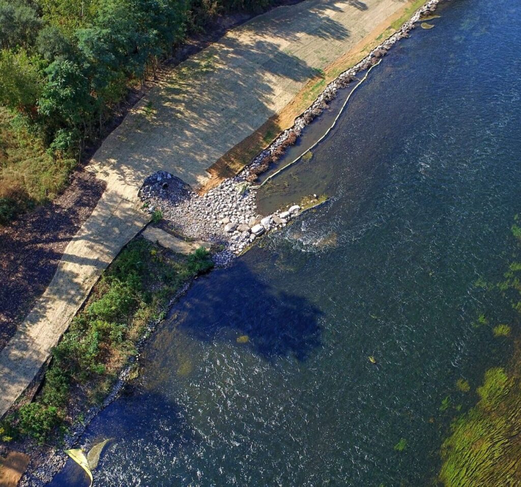 Aerial view of a river showing a degraded spot in the riverbank where boulders are eroding into the water.
