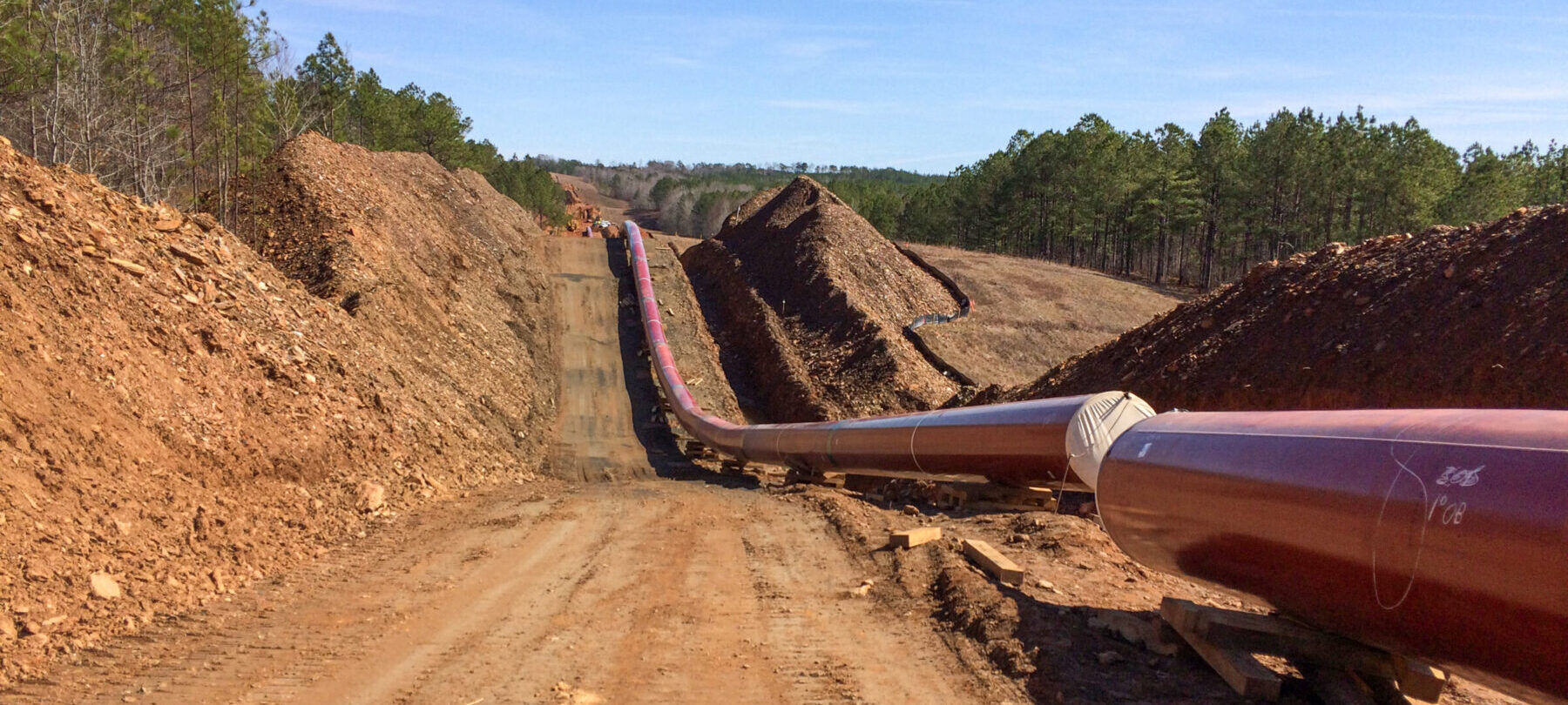 An above-ground natural gas pipeline is running parallel to the dirt even going up a hill.
