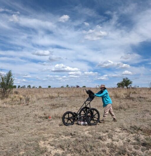 A person pushes a 3-wheeled ground-penetrating radar machine over arid land.