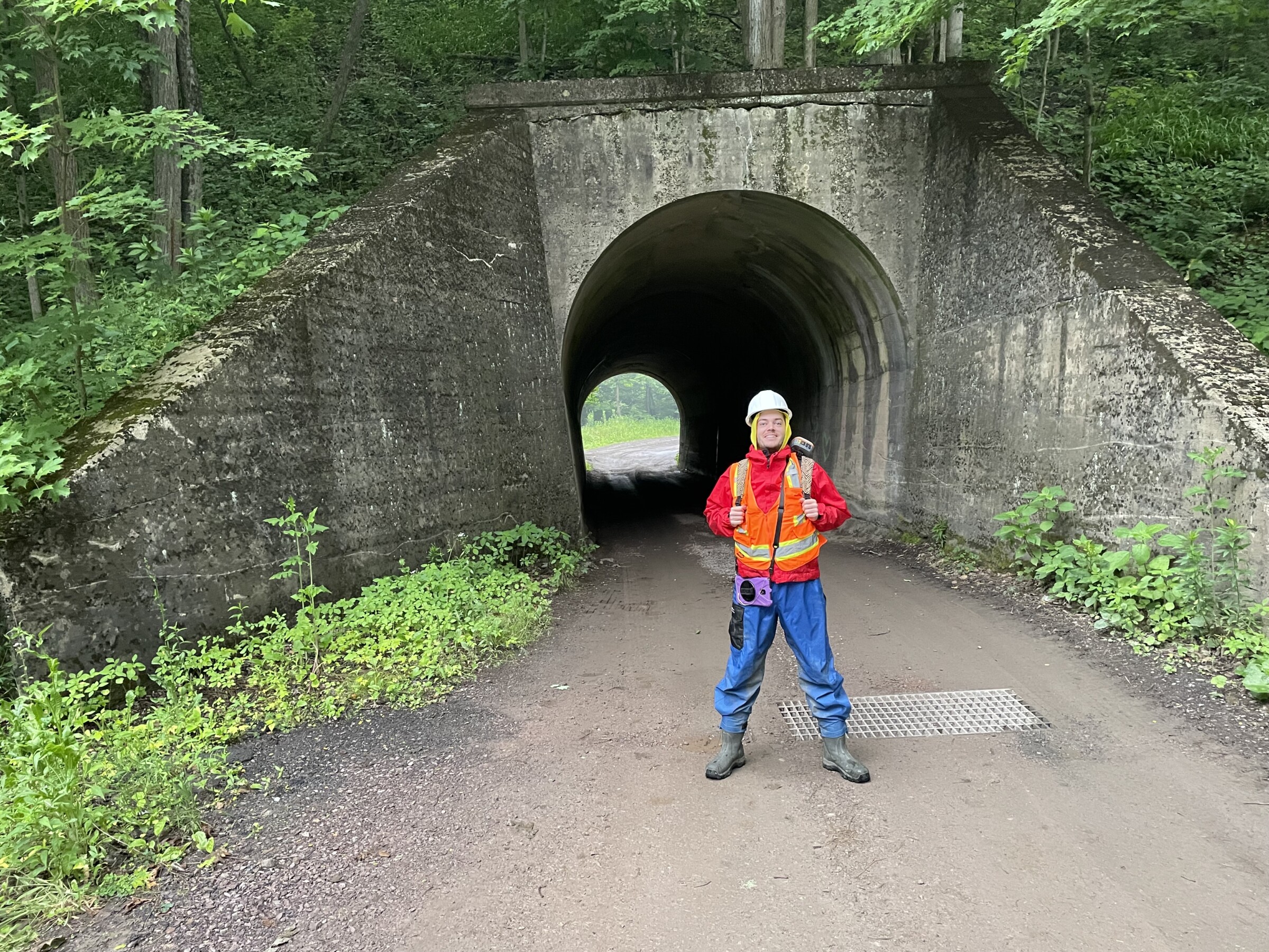 A person in an orange safety vest standing in front of a tunnel.