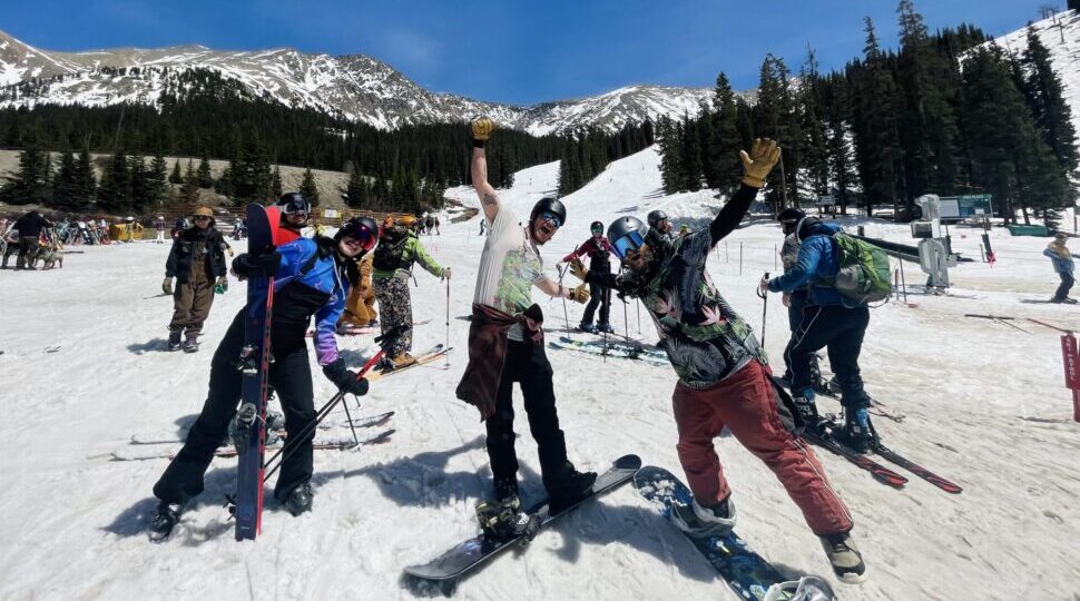 Group of about ten people with snowboards and skis enjoy their time on a snow-covered mountain.