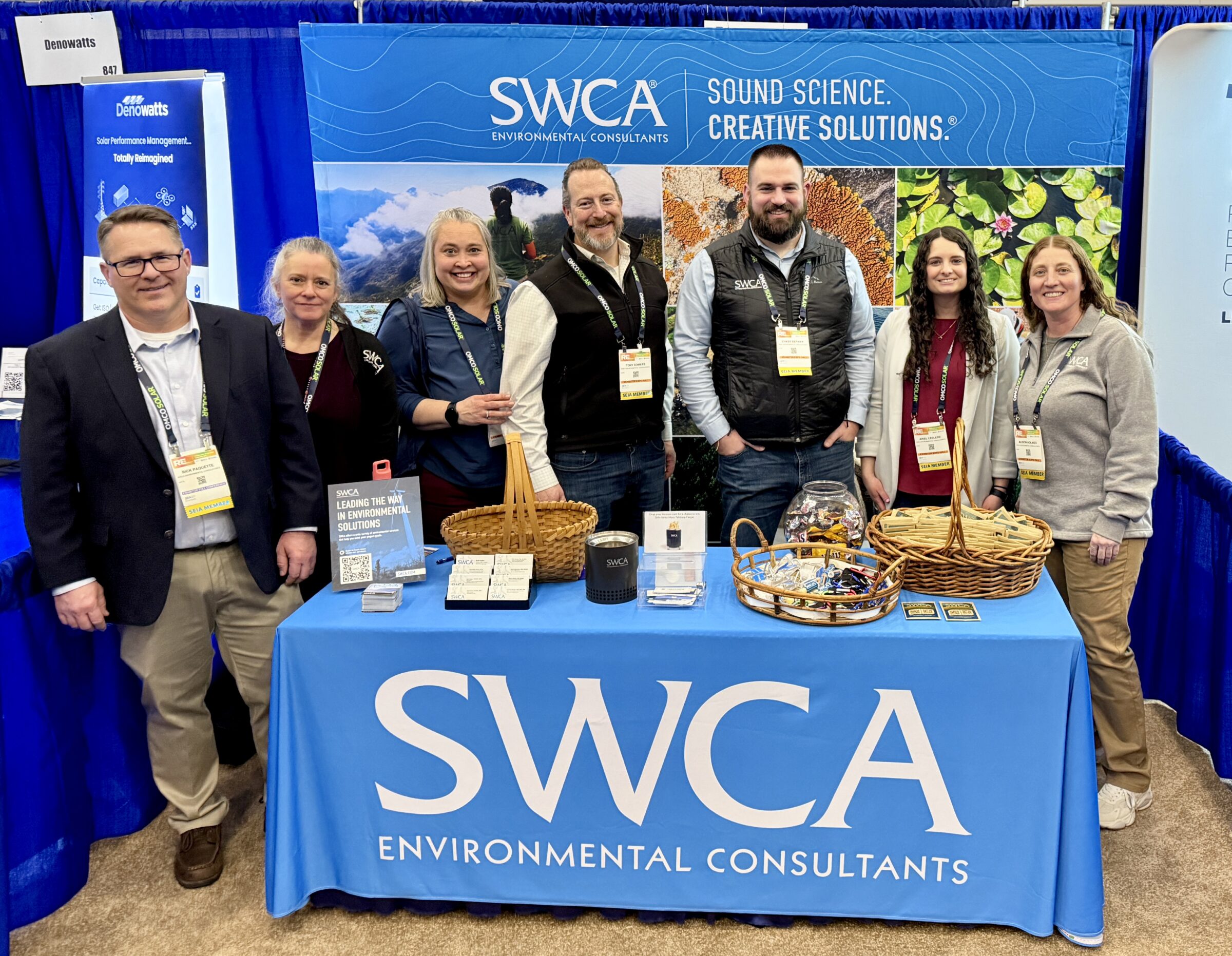 Conference booth branded for SWCA. Seven people with name badges around their necks pose for group photo.