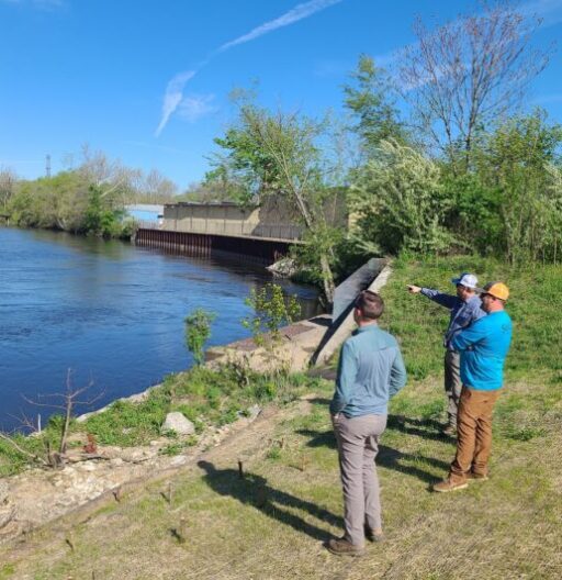 Three people standing near an embankment of water with a cement building nearby.