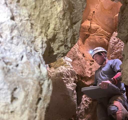 A field technician inspecting a cave wall using a headlamp on his hard hat.