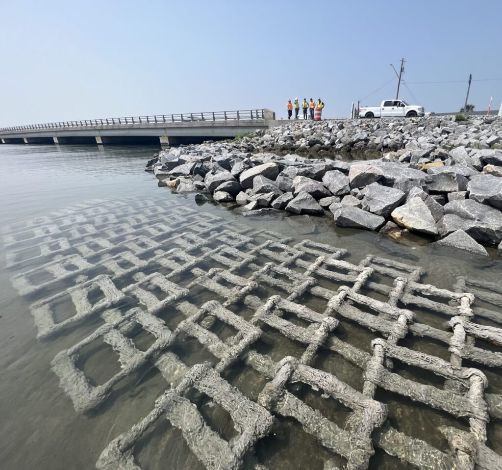 Wave attenuation devices installed in a body of water near a bridge and riprap rocks near the shoreline.