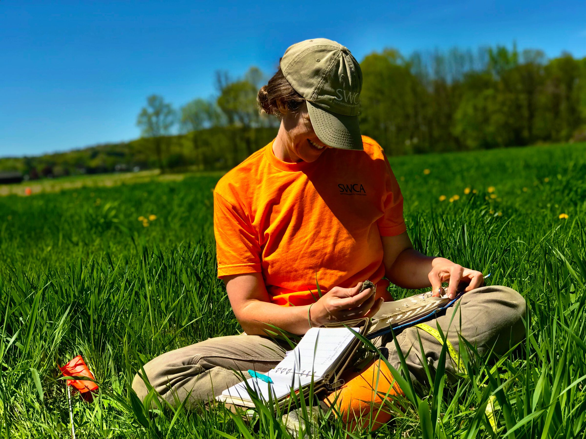 One person sitting cross legged in a field of green grass, working on a paper notebook.