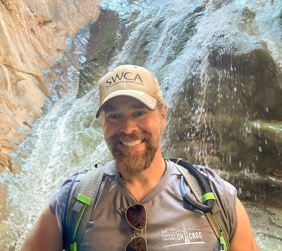 Joseph Fluder on a hike posing by a waterfall.