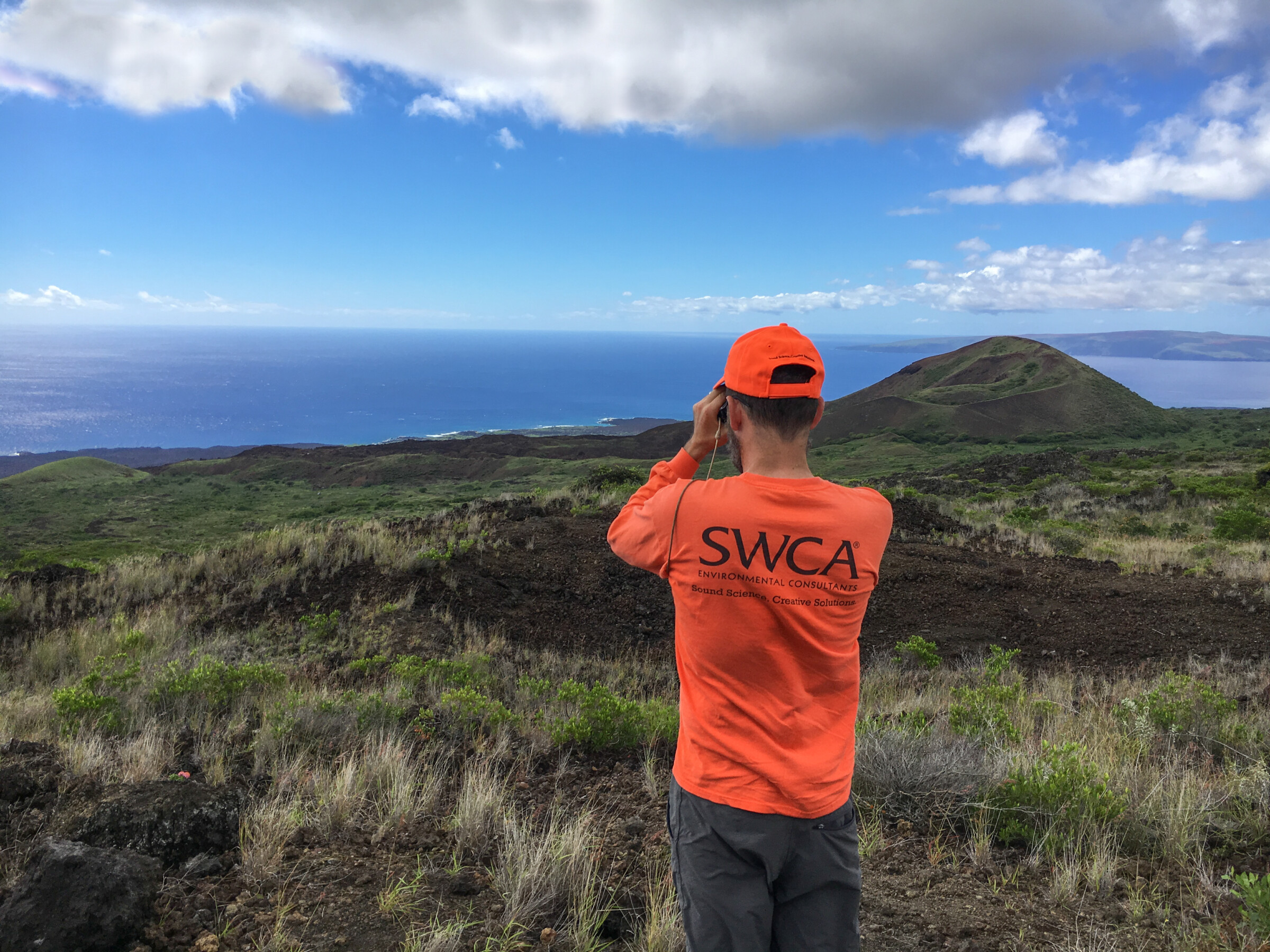 A field biologist wearing an orange SWCA shirt is looking out to the shore near East Maui, Hawaii.