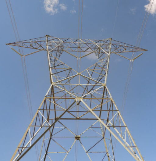 View of an electric transmission tower from the ground, looking at its profile.
