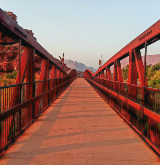 Low-angle view from the edge of a suspension footbridge at sunset, receding into the distance.