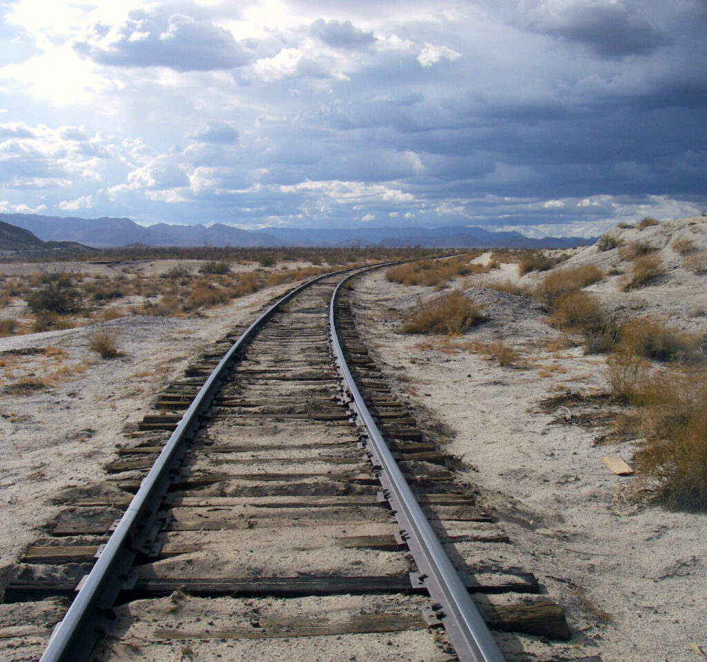Railroad tracks in an open desert receding to the horizon on a cloudy day.