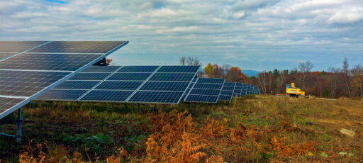 Low angle view of a solar panel array installed in a cleared field, with a construction vehicle in view.