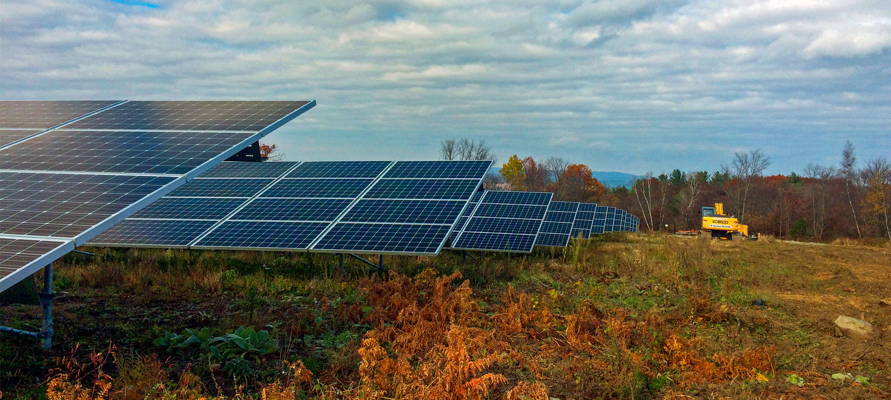Low angle view of a solar panel array installed in a cleared field, with a construction vehicle in view.