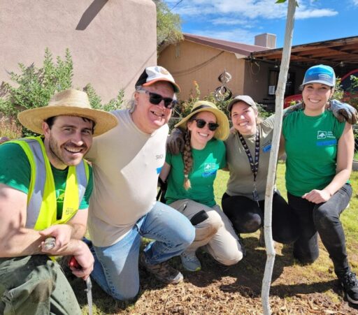 Five people kneel in the mulch for a group photo on a bright sunny day.