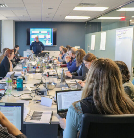 Conference room table with about 12 people attending a lecture, everyone with laptops open.